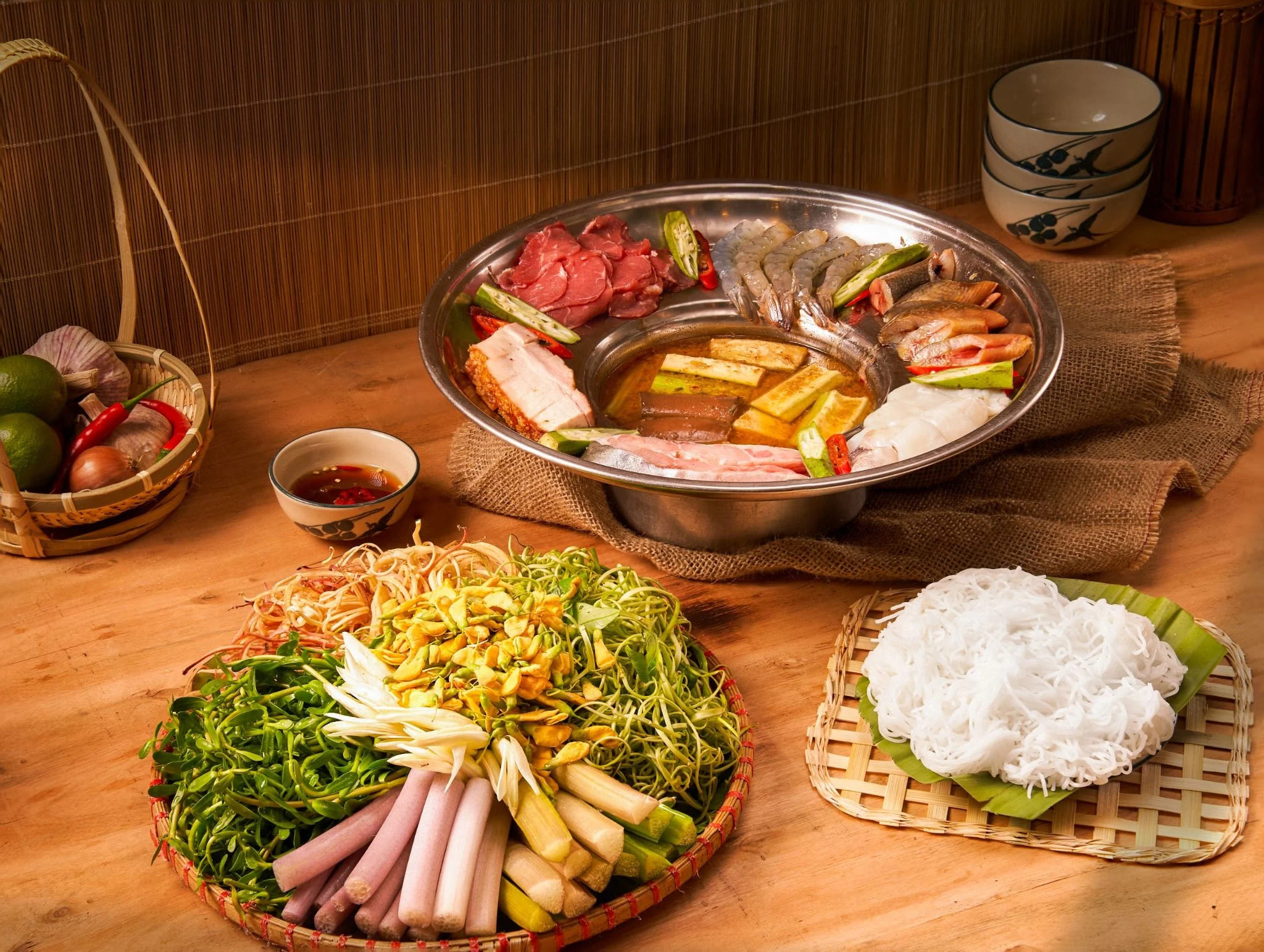 Nồi lẩu mắm miền Tây nghi ngút khói với rau đồng bông súng, kèo nèo và cà tím xung quanh, cùng tô bún tươi trụng sơ