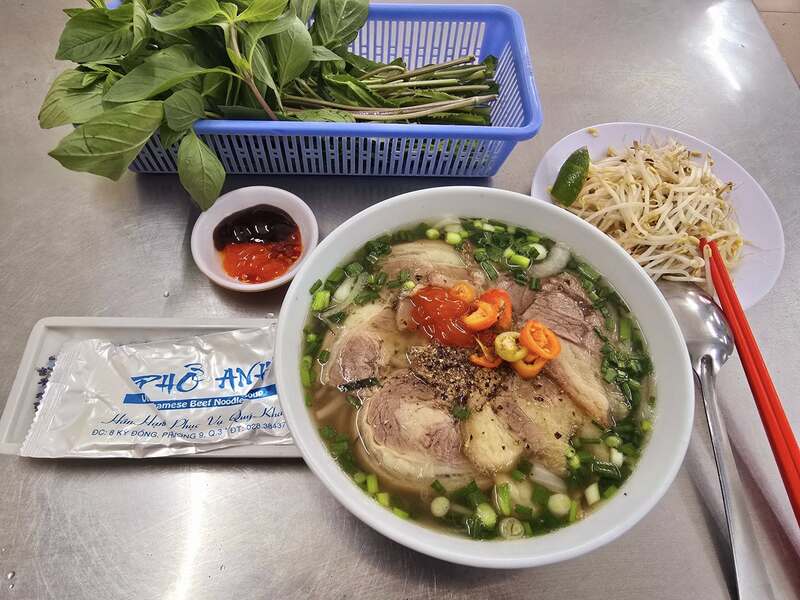 Tô phở miền Nam tại Phở Hòa Pasteur — nước dùng trong ngọt, đĩa rau thơm đầy ắp và chén tương đen tương đỏ đặc trưng Sài Gòn